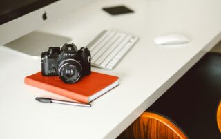 DSLR-Kamera liegt neben einem roten Notizblock auf einem Schreibtisch